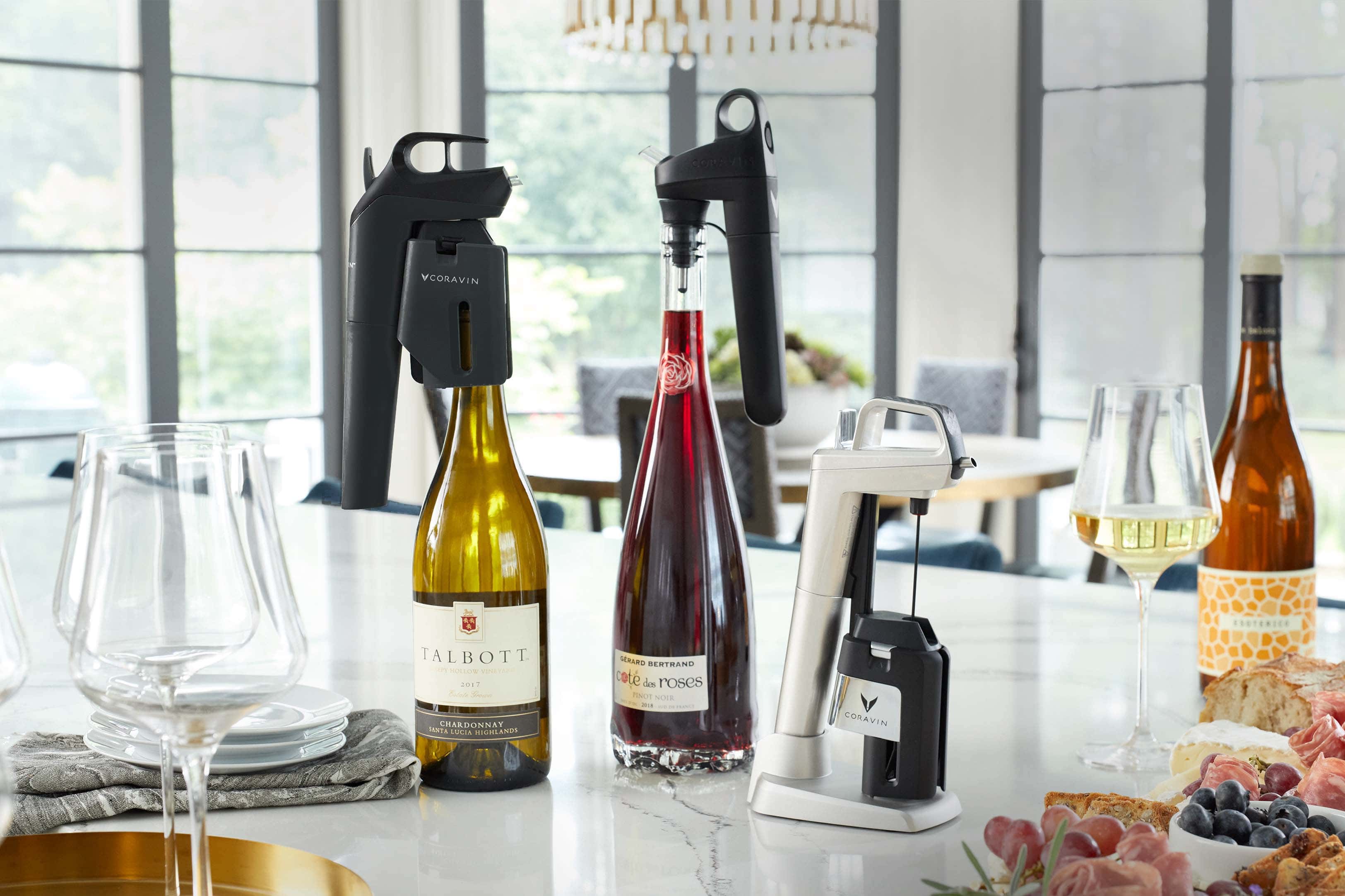 Coravin wine preservation systems displayed on a modern kitchen counter with bottles of red and white wine, wine glasses, and a charcuterie board.