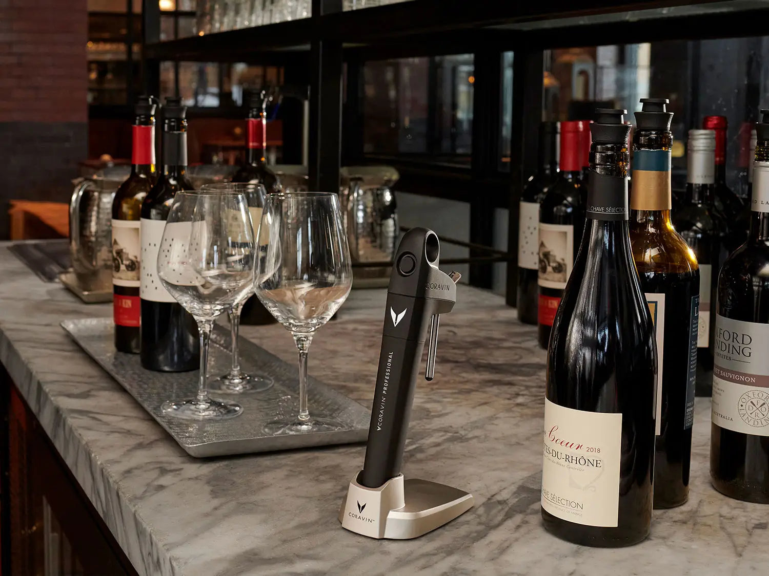 Wine bottles and glasses on a marble bar counter, featuring a Coravin wine preservation system.