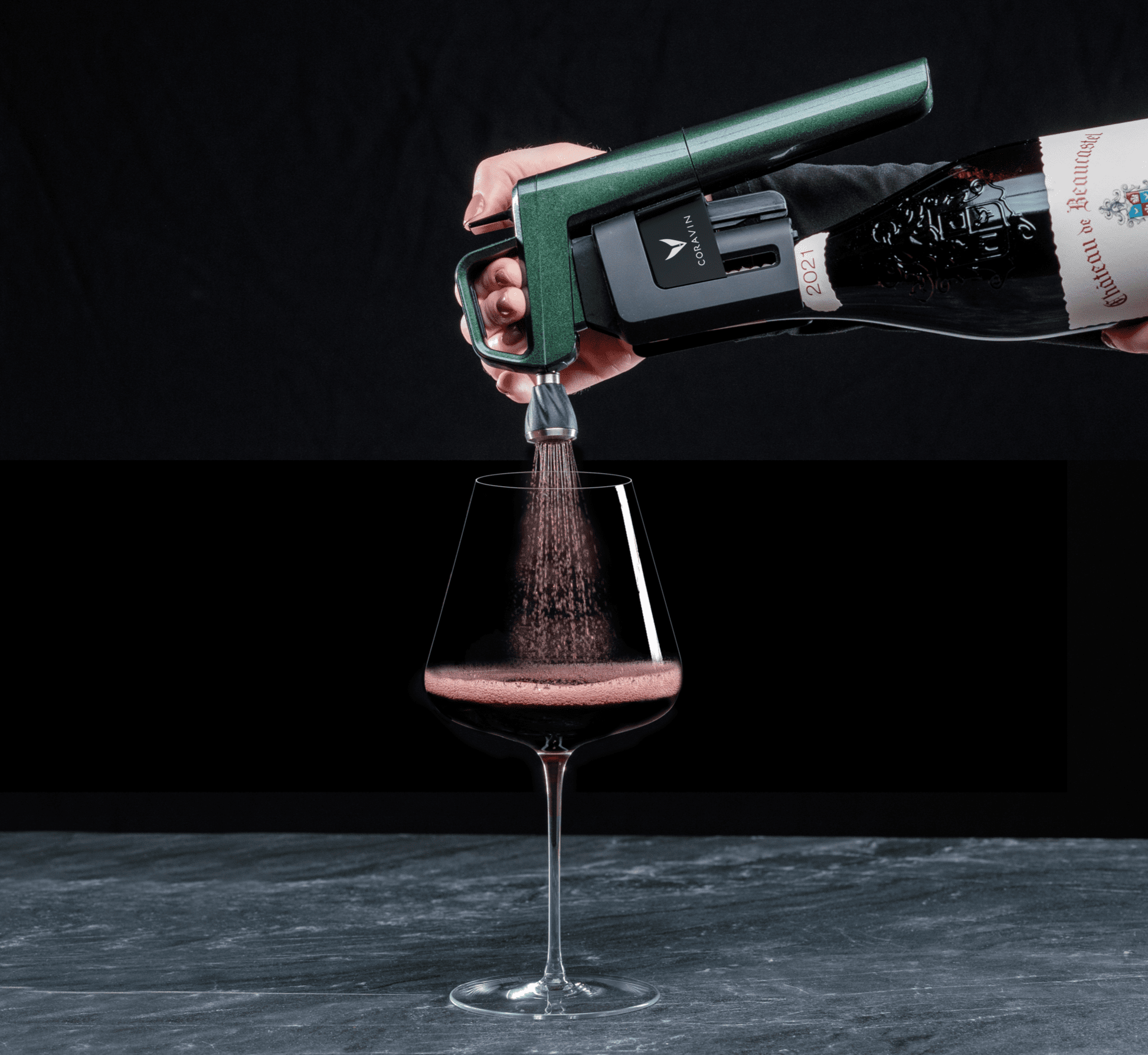 A green wine aerator pours red wine into a large glass, creating a frothy surface against a black background.
