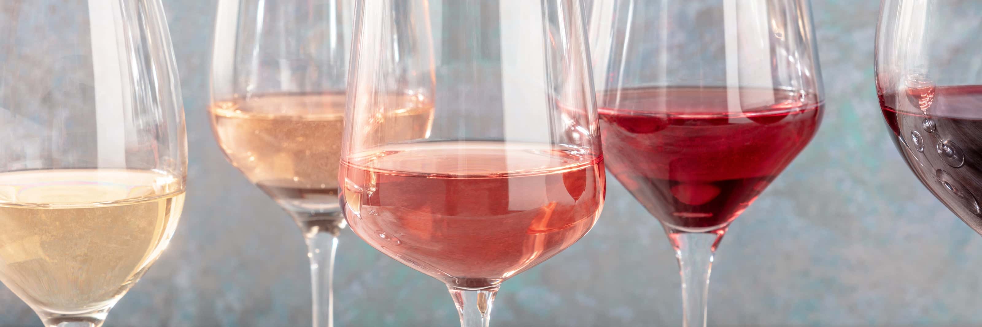 Close-up of wine glasses filled with white, rosé, and red wines, showcasing a colorful variety of wine styles on a textured background.