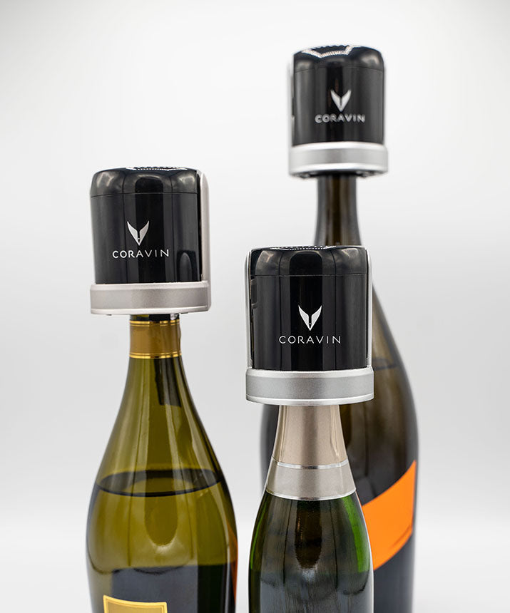 Three wine bottles with Coravin wine preservation systems caps on top. One bottle features a bright orange label.